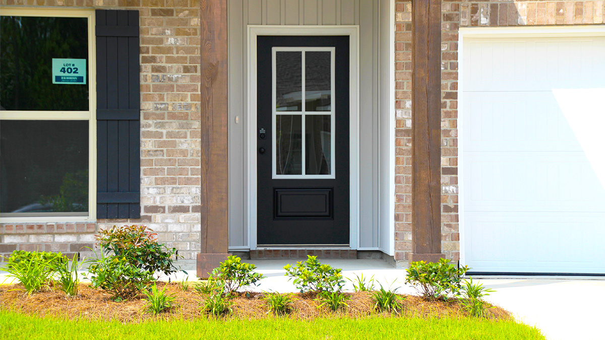 Single-story home with brown brick. Black glass front door with navy shutters and white two car garage.