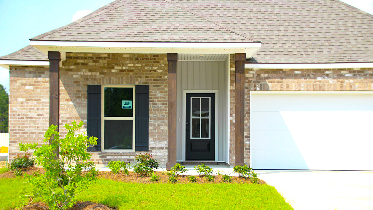 Single-story home with brown brick. Black glass front door with navy shutters and white two car garage.