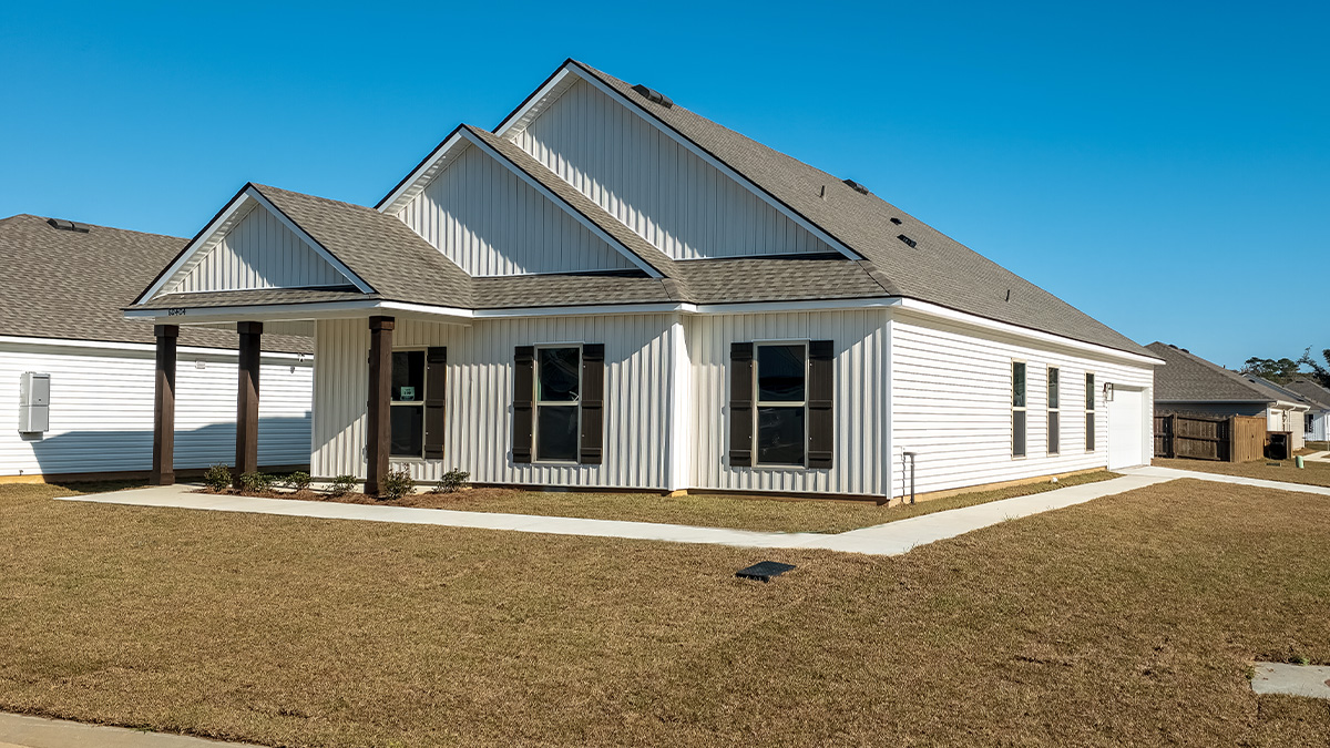 Single-story home with light tan vinyl siding and brown front door and shutters with porch and two-car garage