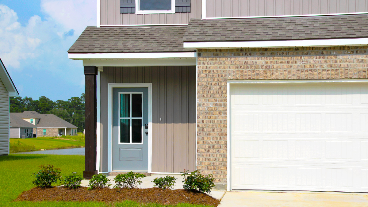 Two-story home with tan hardie vinyl and tan brick. Blue glass front door with brown shutters and white two car garage.