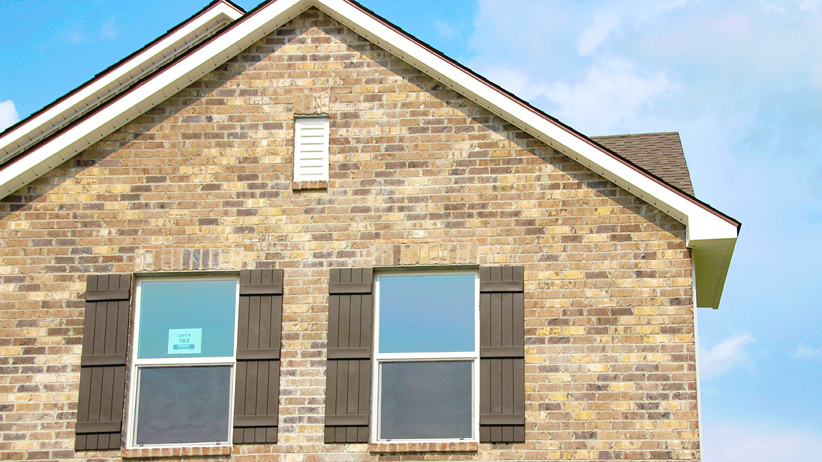 Two-story home with cream hardie vinyl and brown brick. Brown glass front door with brown shutters and white two car garage.