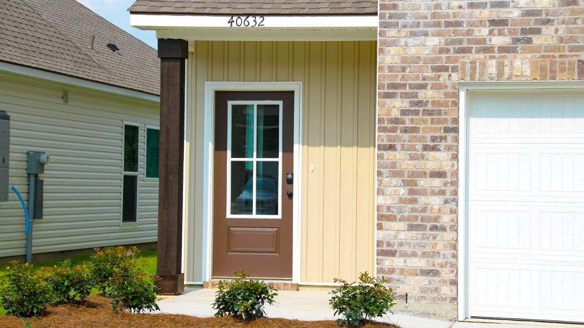 Two-story home with cream hardie vinyl and brown brick. Brown glass front door with brown shutters and white two car garage.