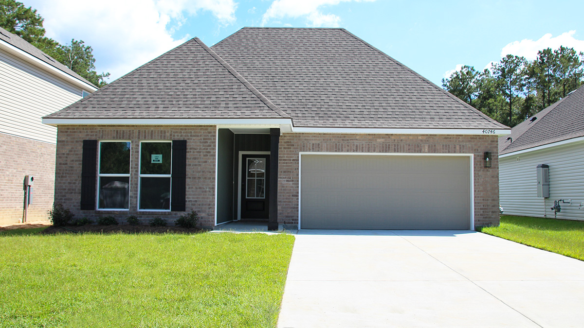 Single-story home with brown brick. Black glass front door with black shutters and white trim and dark green vinyl.