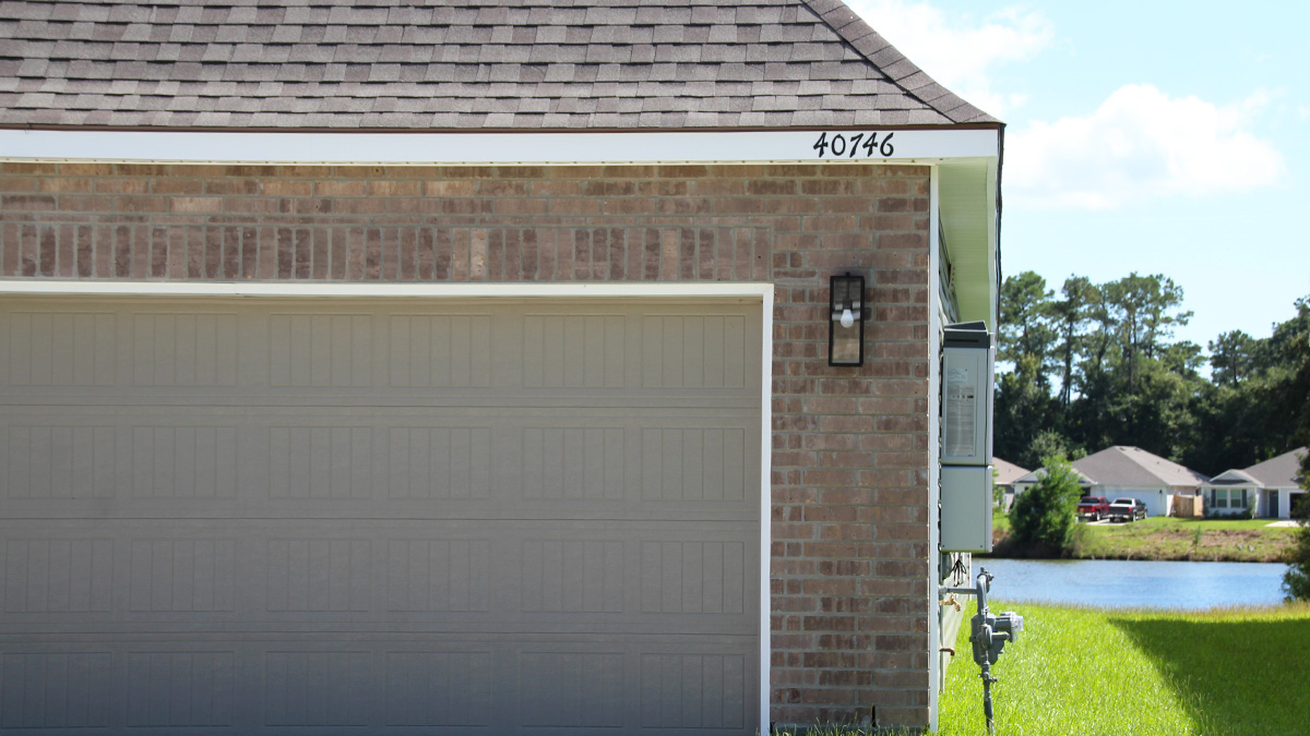 Single-story home with brown brick. Black glass front door with black shutters and white trim and dark green vinyl.
