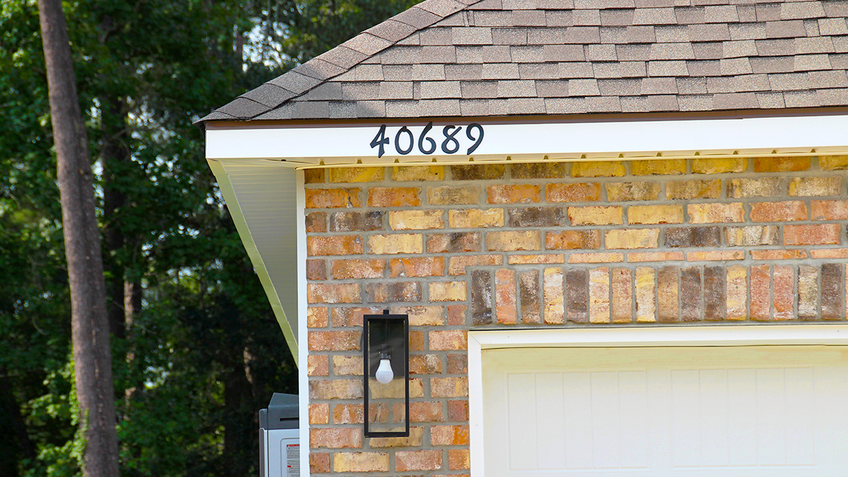 Single-story home with brown brick and white hardie vinyl. Black glass front door with black shutters and white two car garage.