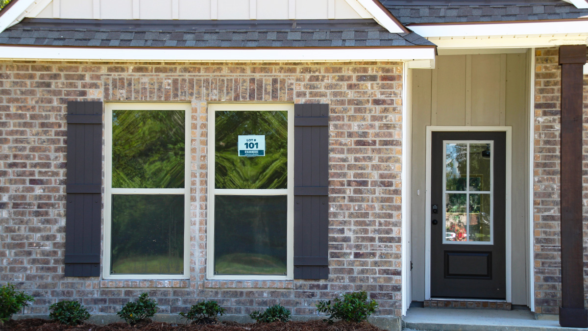 Single-story home with dark grey brick. Dark brown glass front door with black shutters and white trim.