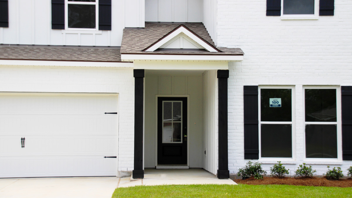 Two-story home with white hardie vinyl and white brick. Black glass front door with black shutters and white two car garage.