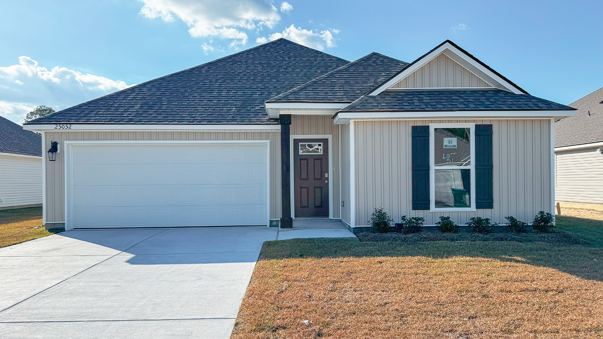 single-story home with tan vinyl siding with brown front door and black shutters with two-car garage