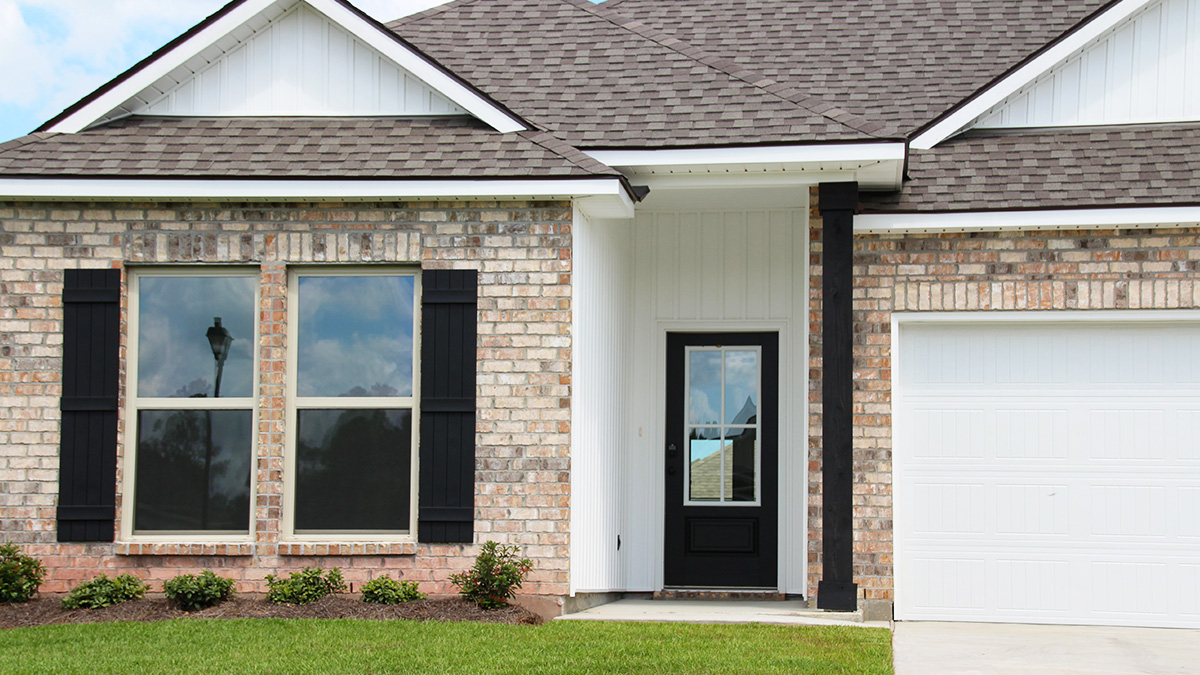 Single-story home with brown brick. Black glass front door with black shutters and white trim.