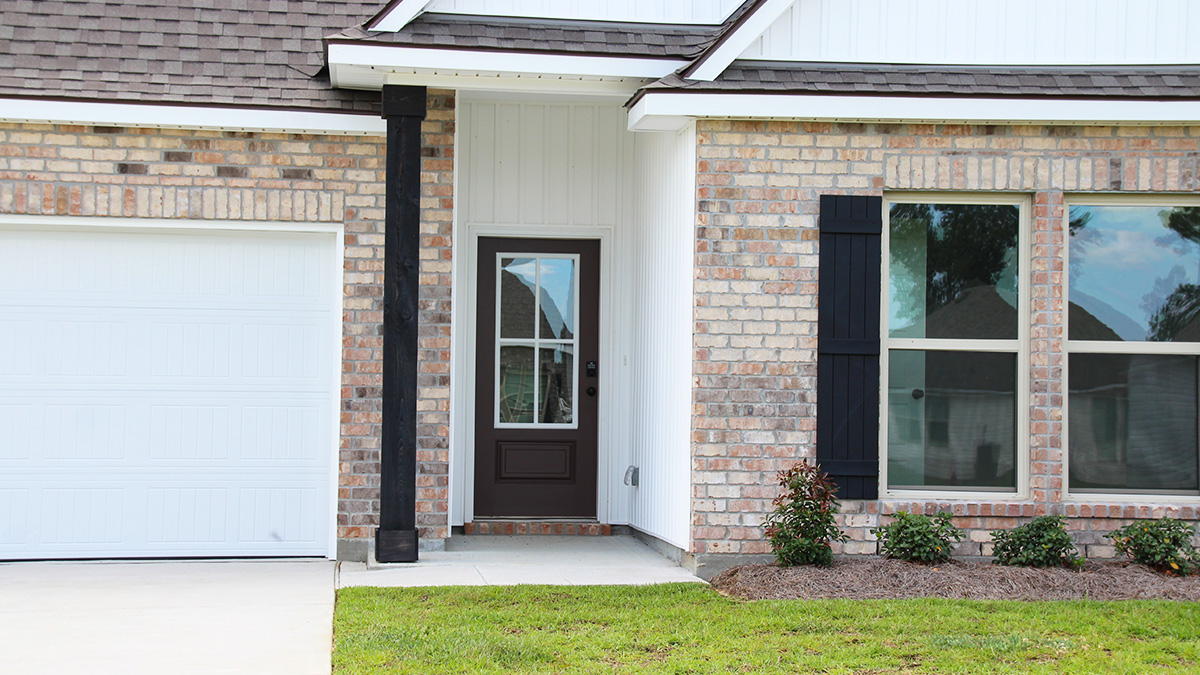 Single-story home with brown brick. Black glass front door with black shutters and white trim.