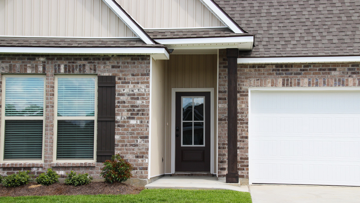 Single-story home with brown brick. Black glass front door with black shutters and white trim.