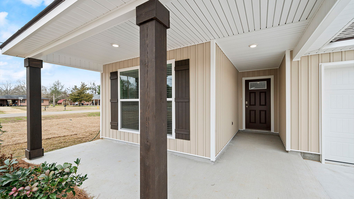 single-story home with tan vinyl siding and brown front door and shutters with porch