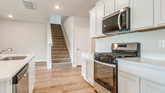 Kitchen with stainless steel appliances, white cabinetry, light wood-type flooring, recessed lighting, and light stone counters