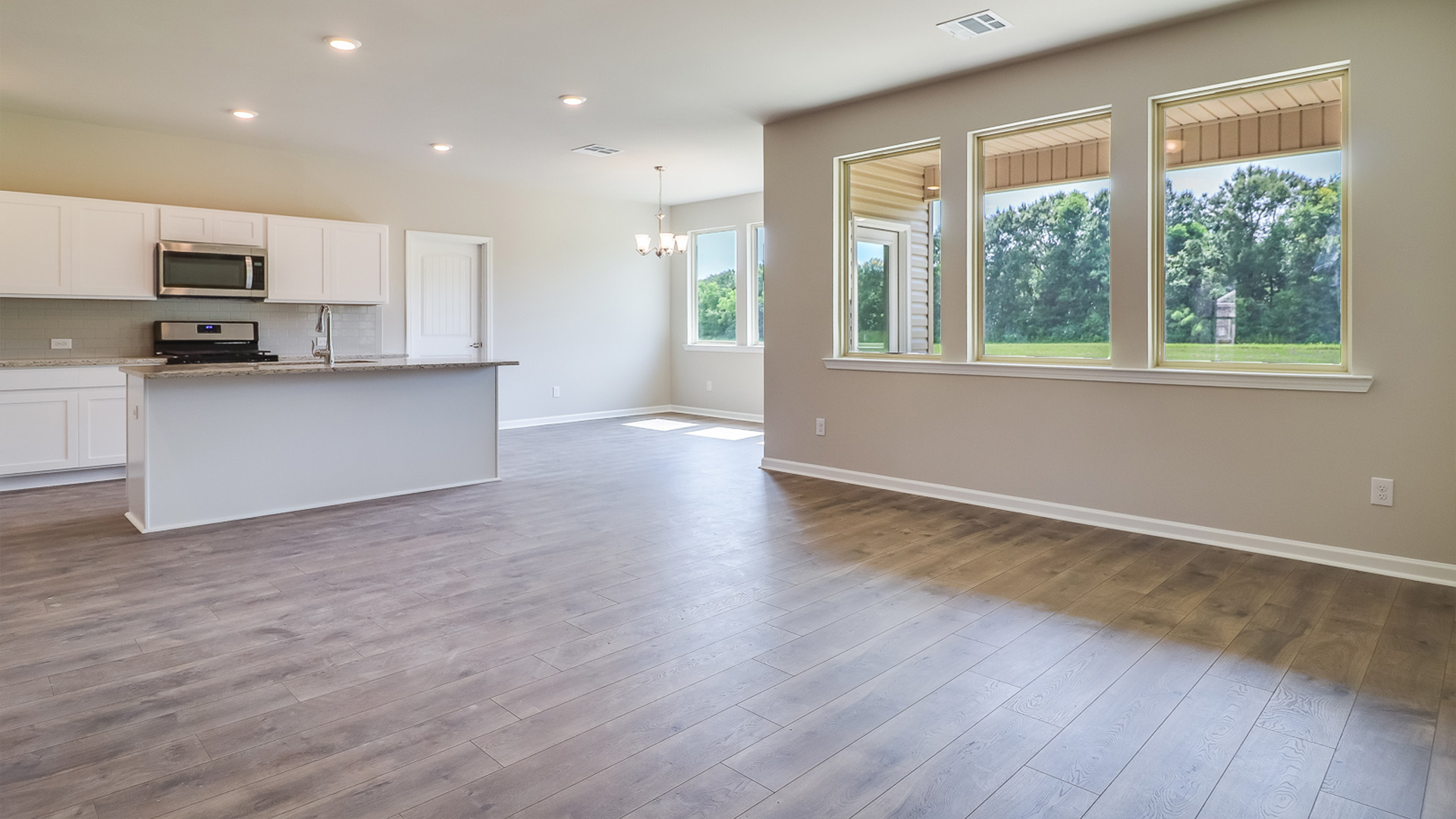 Main living area with clean flooring and natural light connecting to kitchen and dining space.