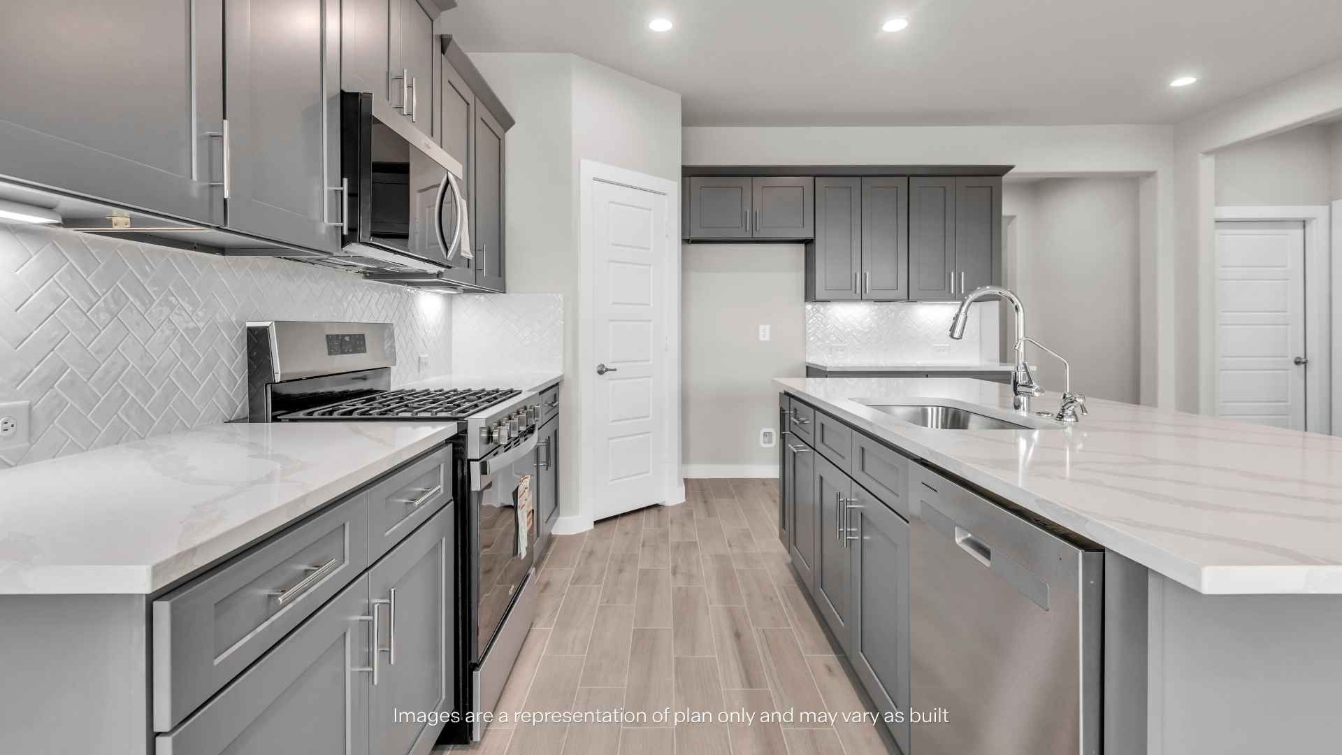 Kitchen with gray shaker-style cabinets, large center island, stainless steel gas range and microwave, white tile backsplash, and quartz-style countertops.