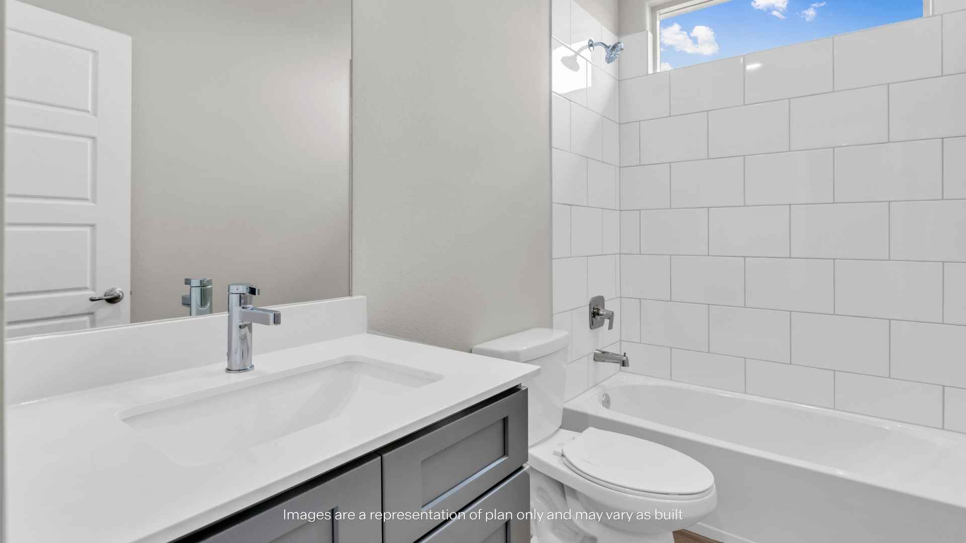 Bathroom with gray vanity cabinet, white countertop, rectangular sink, toilet, and bathtub with white subway tile surround and window above.