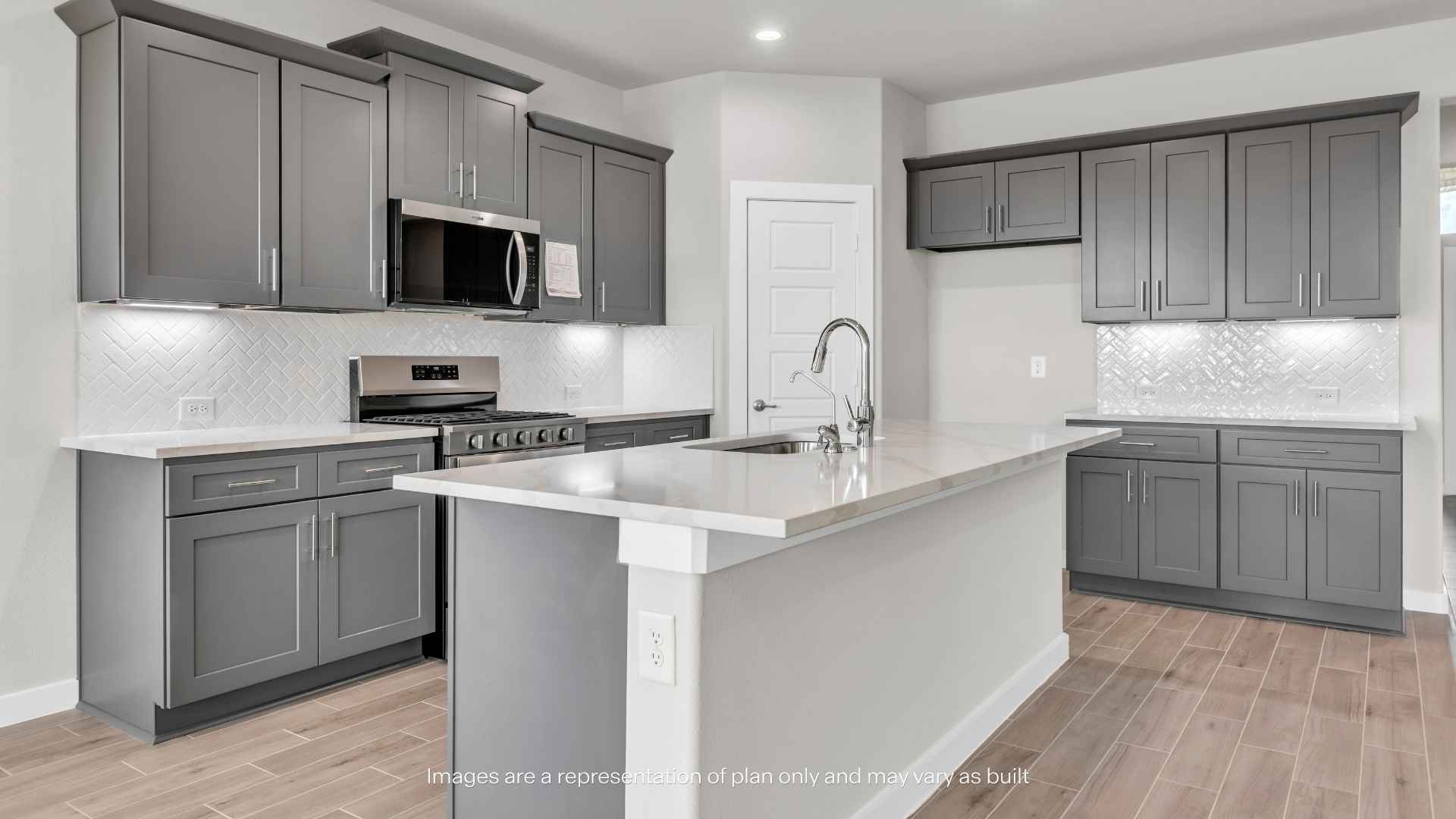 Modern kitchen with gray shaker cabinets, large center island with sink, white countertops, stainless steel appliances, tile backsplash, and wood-look tile flooring.