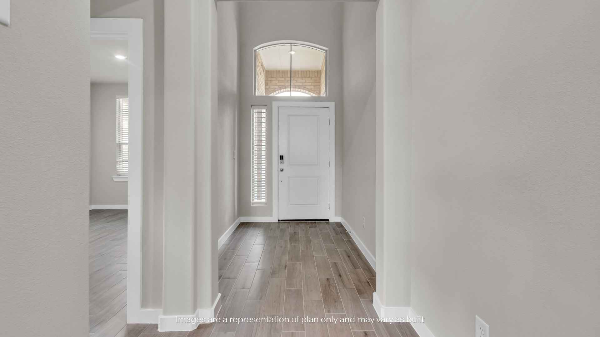 Interior view of the home's entry hallway with wood-look tile flooring, tall ceilings, white front door, and natural light from sidelights and transom window.