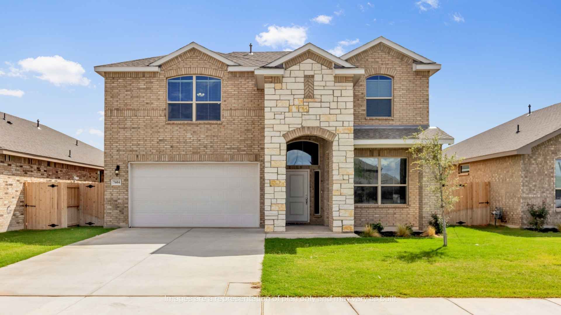 Two-story brick home with stone-accented entryway, two-car garage, paved driveway, landscaped front lawn, and neighboring homes under a clear blue sky.