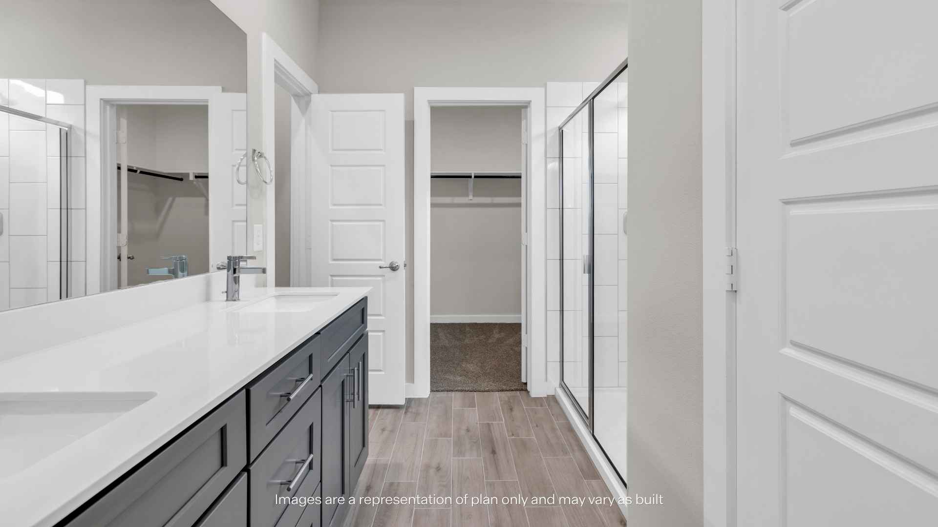 Primary bathroom with dual-sink vanity, glass shower, and walk-in closet access.