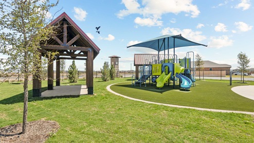 Lush green playground and park area with covered seating and covered play area for residents