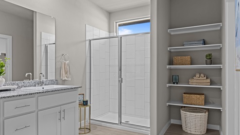 Attached private primary bathroom with elevated tiled shower, built in vanity, and shelving for extra storage space