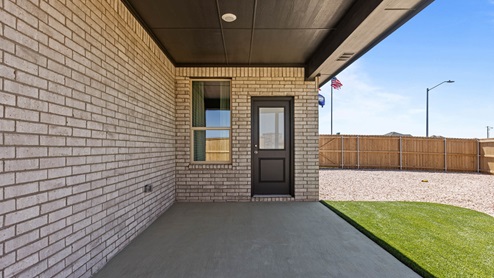 Covered back patio area overlooking spacious backyard with turf and stone landscaping