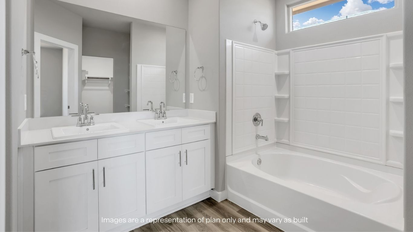 A bright bathroom with dual sinks, a large mirror, and a built-in bathtub with shower.