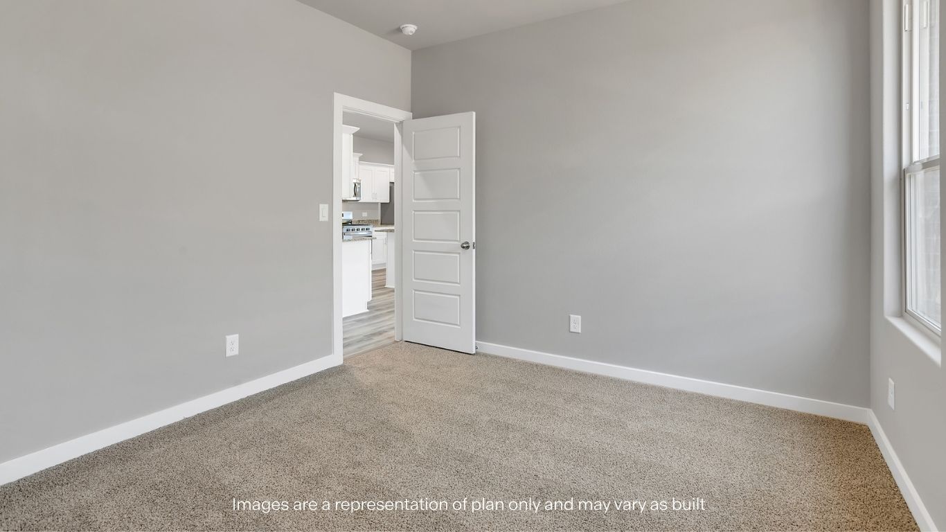 A bright bedroom with soft carpet, light gray walls, and an open door leading into the main living area.