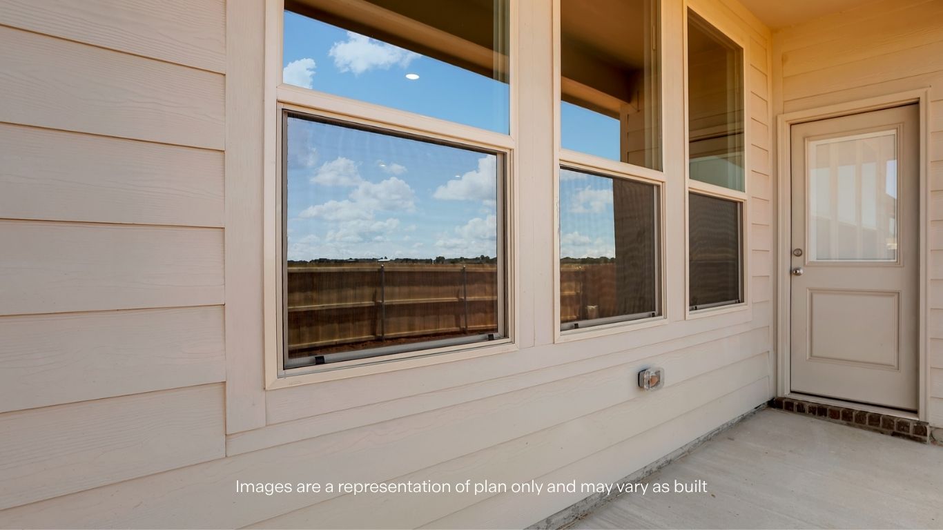 A covered back patio with large windows and a door providing access to the backyard.