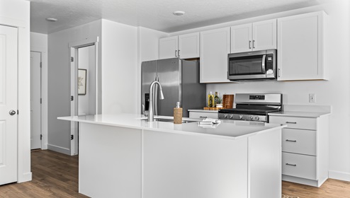 Focusing on the kitchen there is a large island with sink, white shaker cabinets and stainless steel appliances.