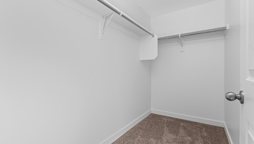 Walk in closet with shelving above wardrobe bars on two sides.
