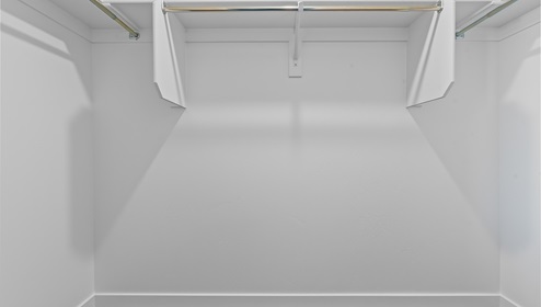 Primary bedroom’s walk in closet with shelving and wardrobe bars on three sides.