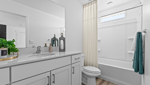 Primary bedroom’s ensuite full size bathroom with white cabinets and tub shower combination.