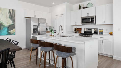 A beautiful kitchen with white shaker cabinets, a large island with sink and stainless steel appliances.