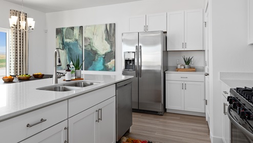 A wide access way through the kitchen flanked with a lot of counterspace, a large kitchen island, white shaker cabinets and stainless steel appliances.