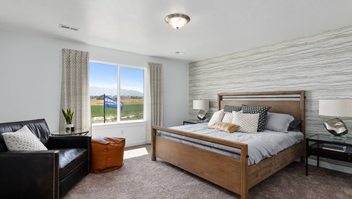 The primary bedroom suite at the Clover floor plan in Little Valley Gateway with a large window and spacious enough for a large bed, side tables on either side and a sitting area.