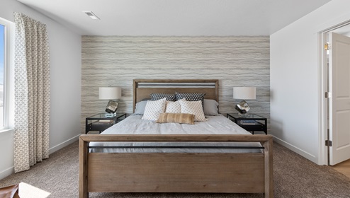 Another view of the primary bedroom looking straight on to the large bed and side tables on either side and large window on the left.
