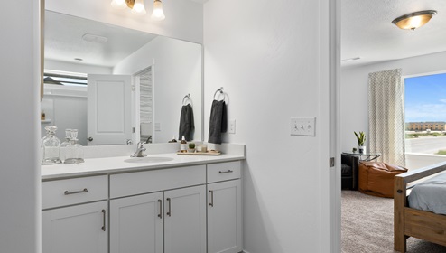 The primary bathroom with one sink and plenty of counter space donned with several white cabinets for organizing and a wide wall to wall mirror.