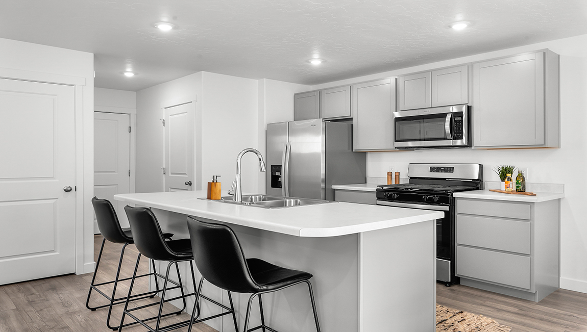 Focusing on the kitchen there is a large island with sink, white shaker cabinets and stainless steel appliances.