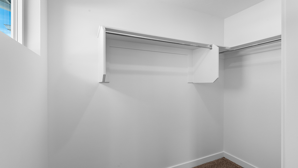 Primary bedroom’s walk in closet with shelving and wardrobe bars on three sides.
