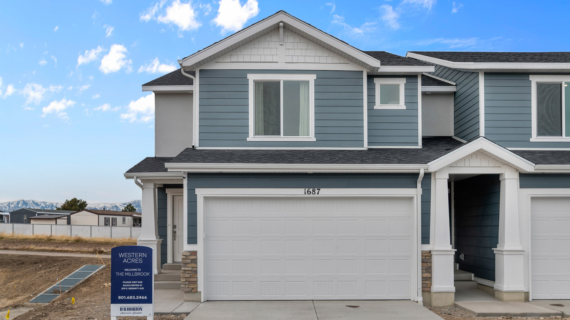 New two-story farmhouse style townhome in Toole Utah with taupe and white colored siding and white trim and a covered porch with a two car garage.