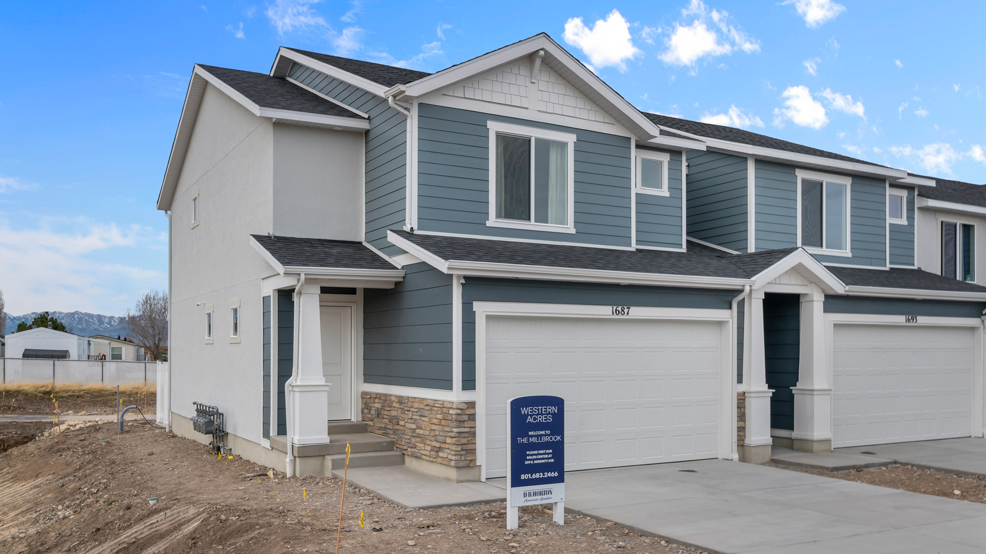 New two-story farmhouse style townhome in Toole Utah with taupe and white colored siding and white trim and a covered porch with a two car garage.