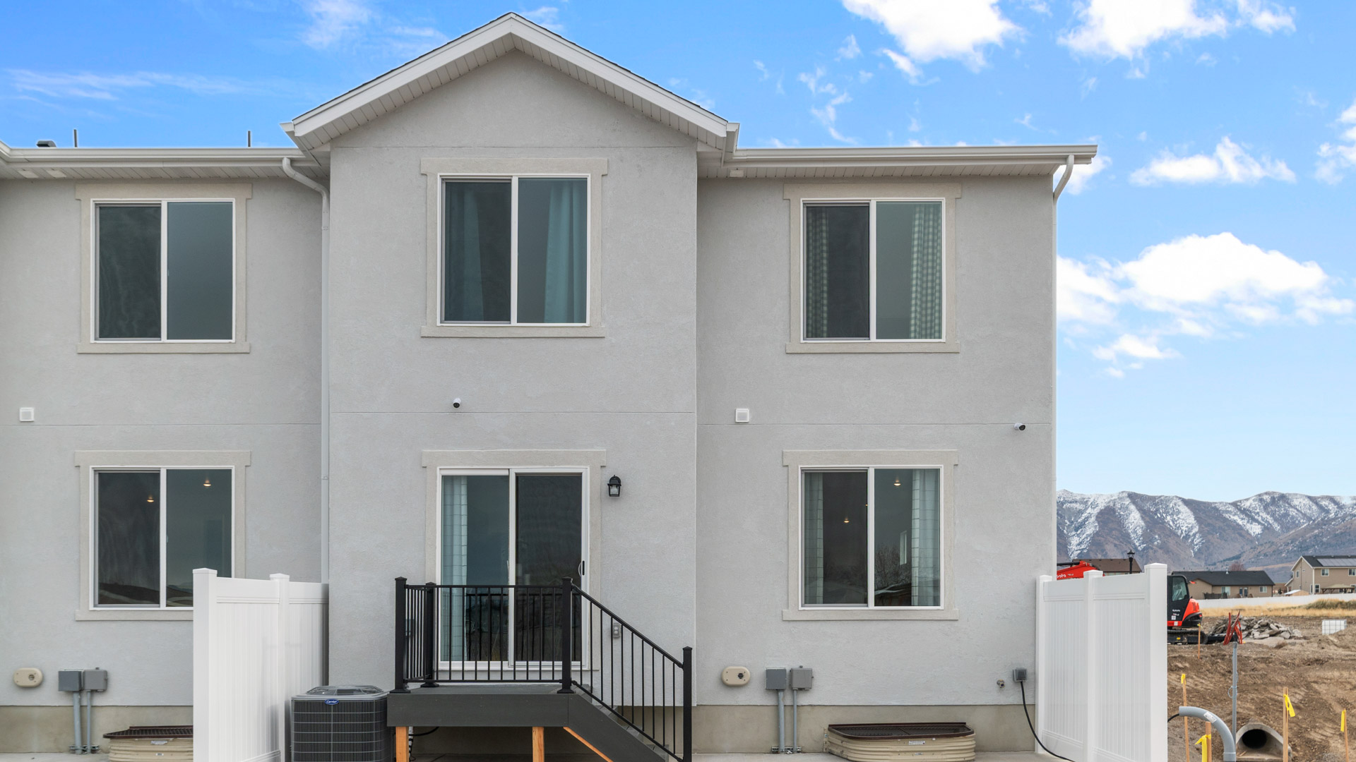 New two-story farmhouse style townhome in Toole Utah with taupe and white colored siding and white trim and a covered porch with a two car garage.