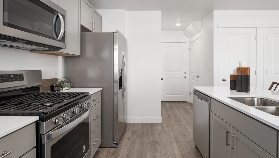 Open alleyway kitchen with stainless steel appliances leading towards the powder room and garage entry.