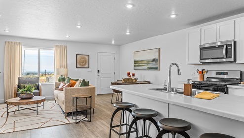 View of the open concept main floor at the Western Acres community in Tooele Utah from the entryway with view of the kitchen, dining area and living room with a large window for lovely light.