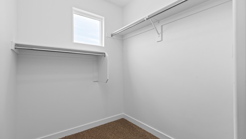 Primary bedroom walk in closet with window and shelves and wardrobe rods on two sides.