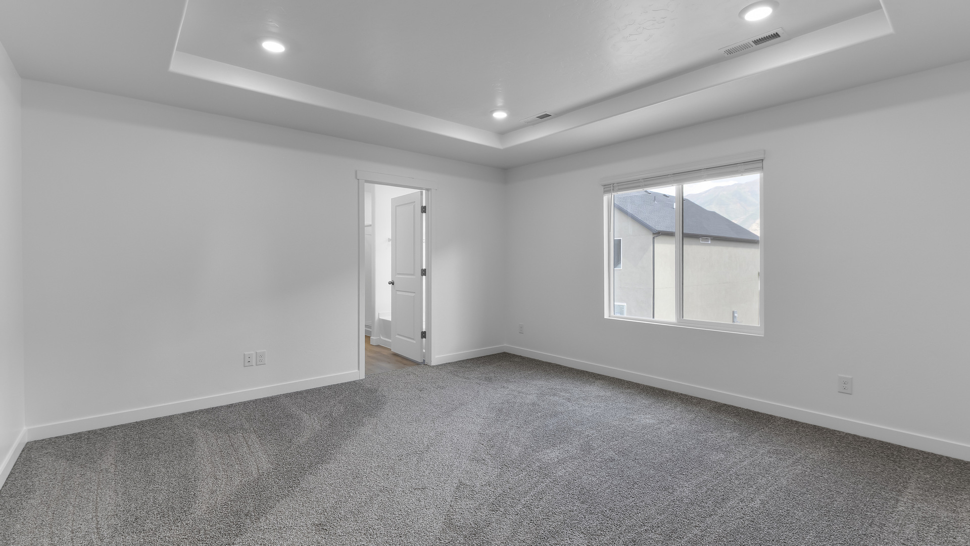 Primary bedroom with tray ceiling and window.