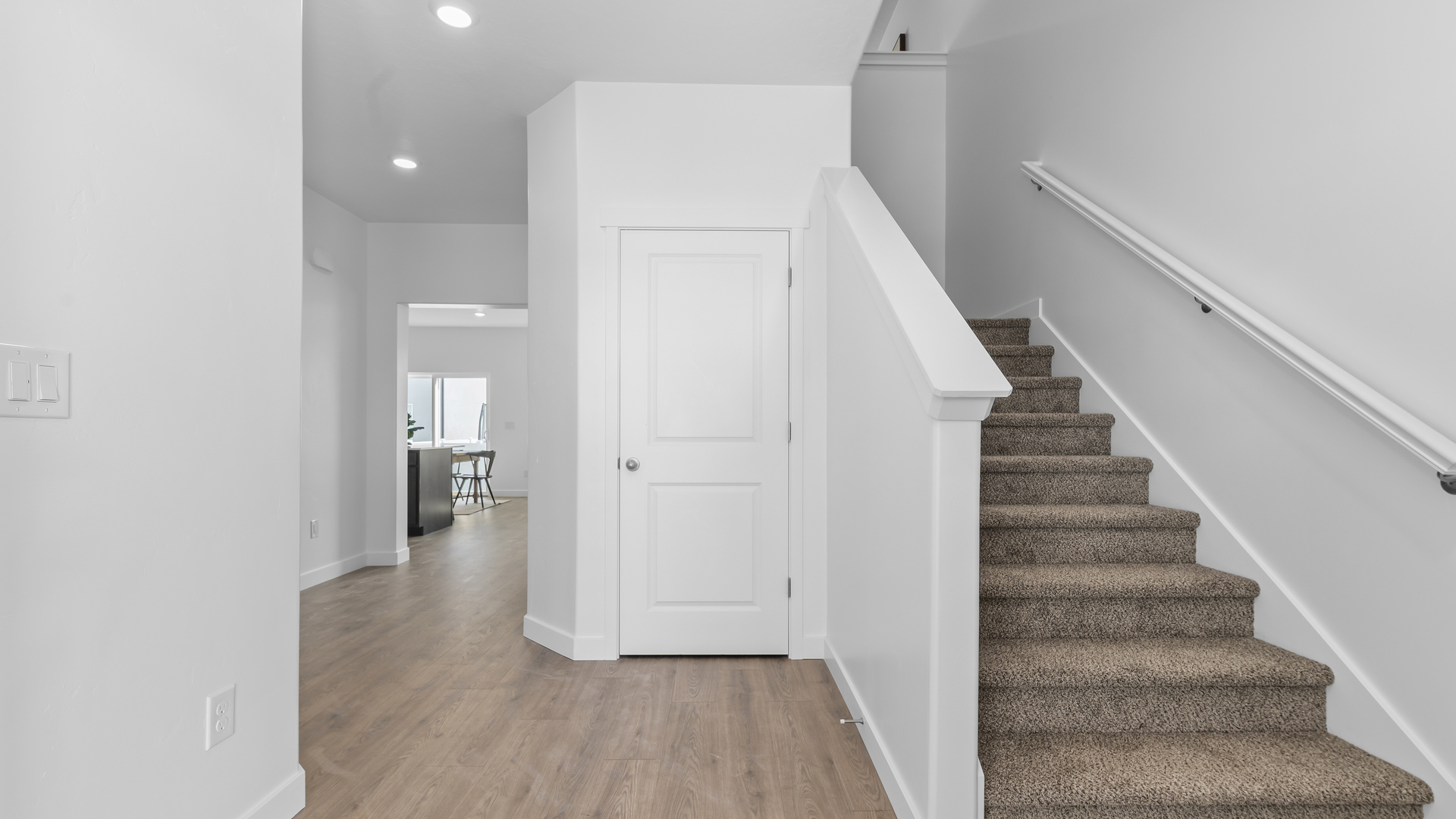 Entryway into the home with two square windows, stairs leading up to the second floor living area and a wide hallway that leads into the main floor living space.