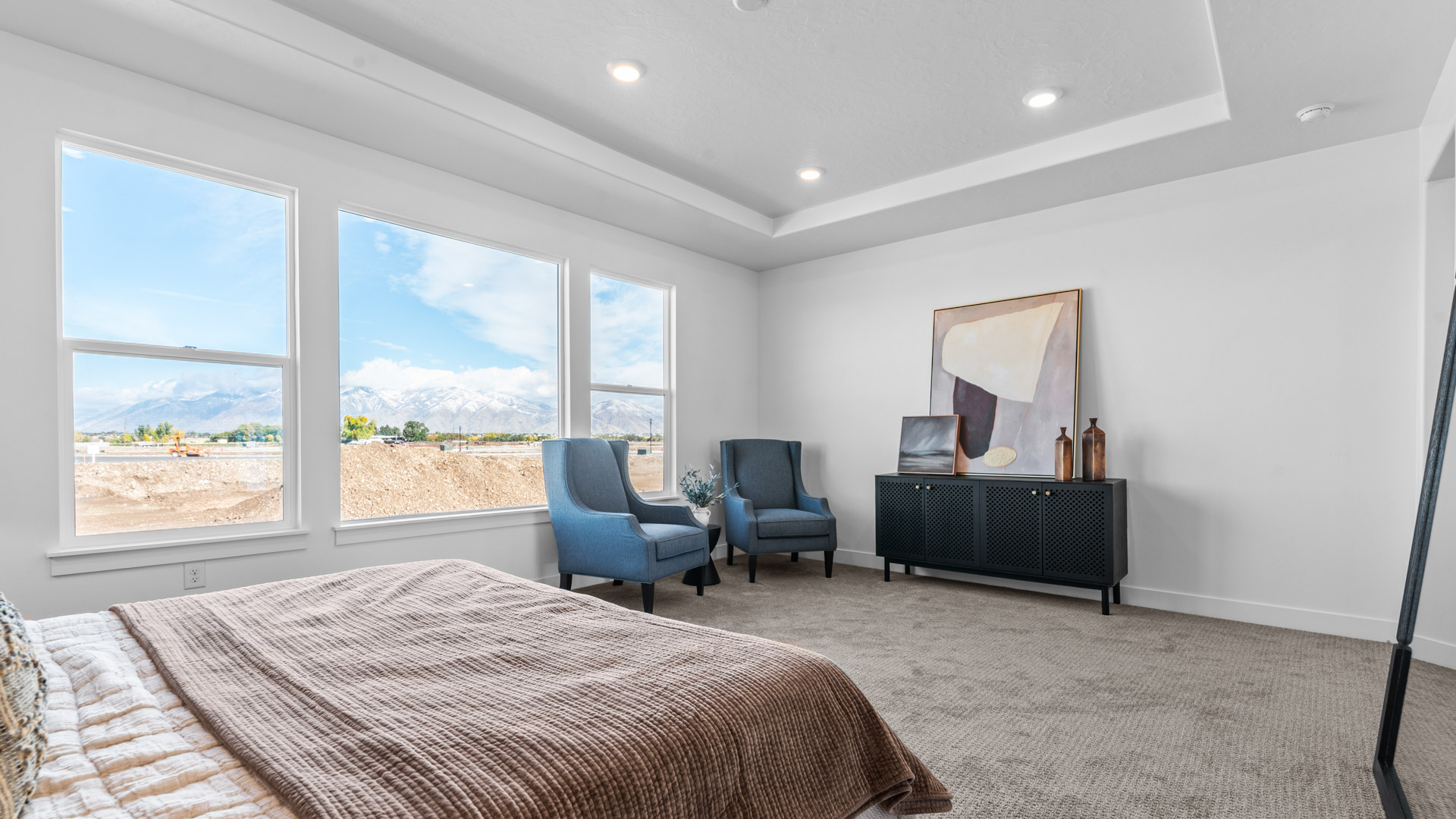 Primary bedroom with tray ceiling and large windows.